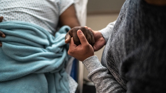 A patient holds the hand of their loved one