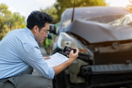 man sitting by a damaged car